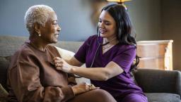 Healthcare provider sitting on a couch with a patient in their home checking their vitals.