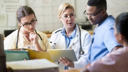 Three healthcare providers sitting together looking at a tablet together