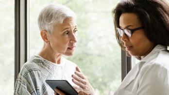 An elderly patient talking to a doctor who is holding a tablet